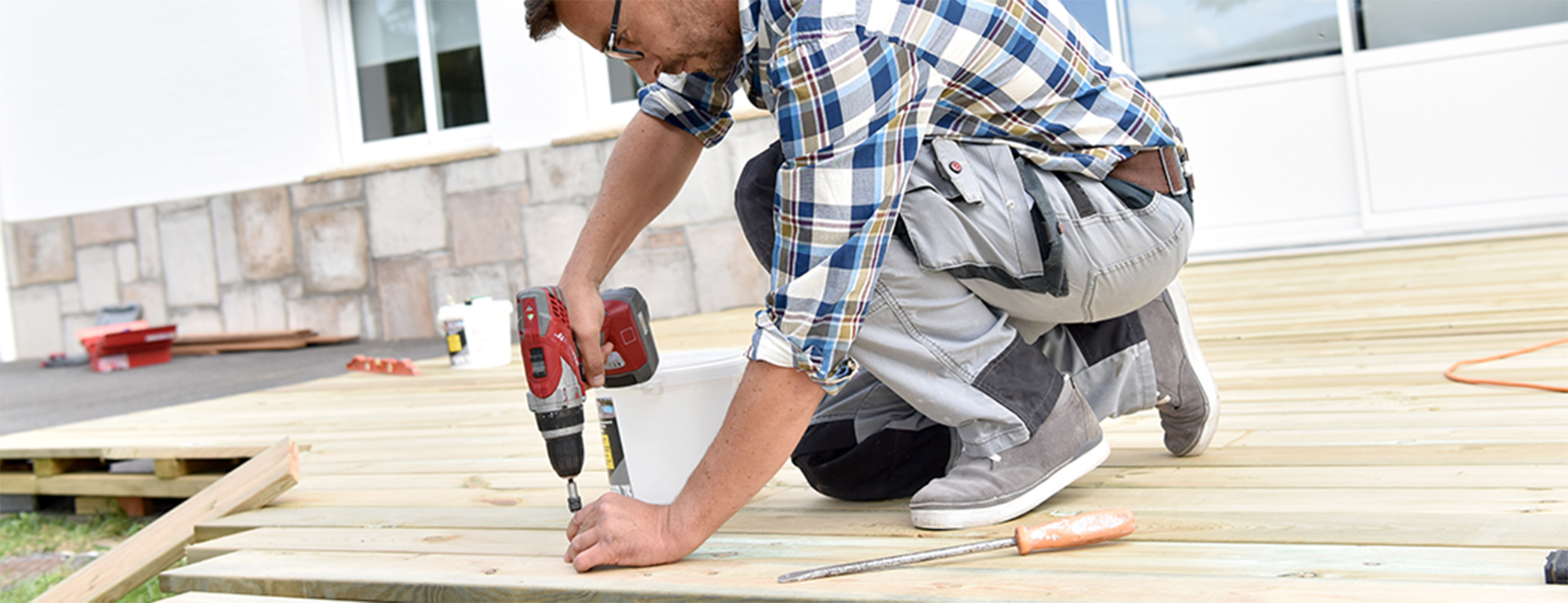 Image of male power-drilling a wood floor outdoors